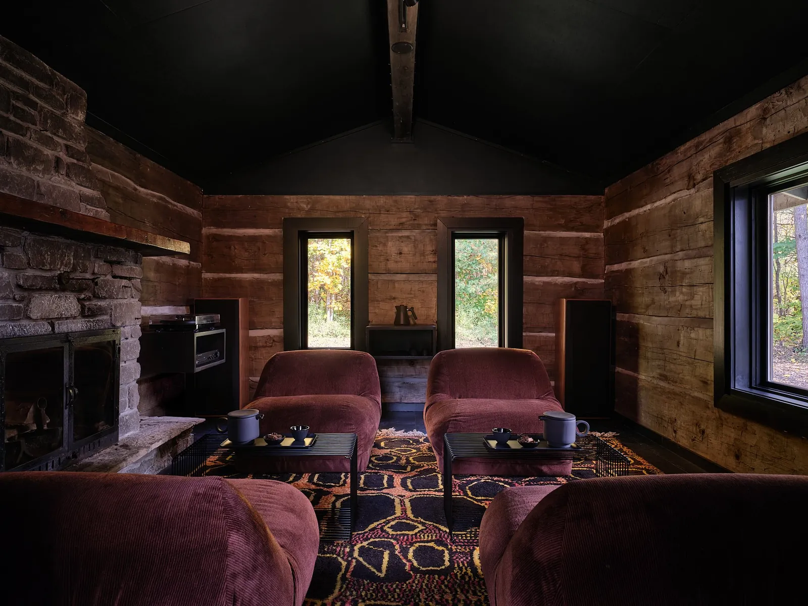 Log-walled room with a stone fireplace, four velvet lounge chairs and a patterned rug