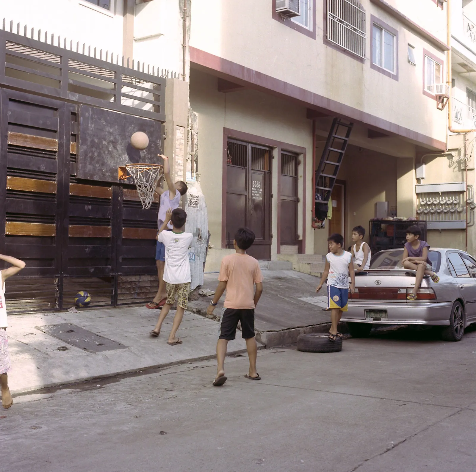 Boys playing basketball on a residential street, shooting at a hoop mounted on a dark metal gate