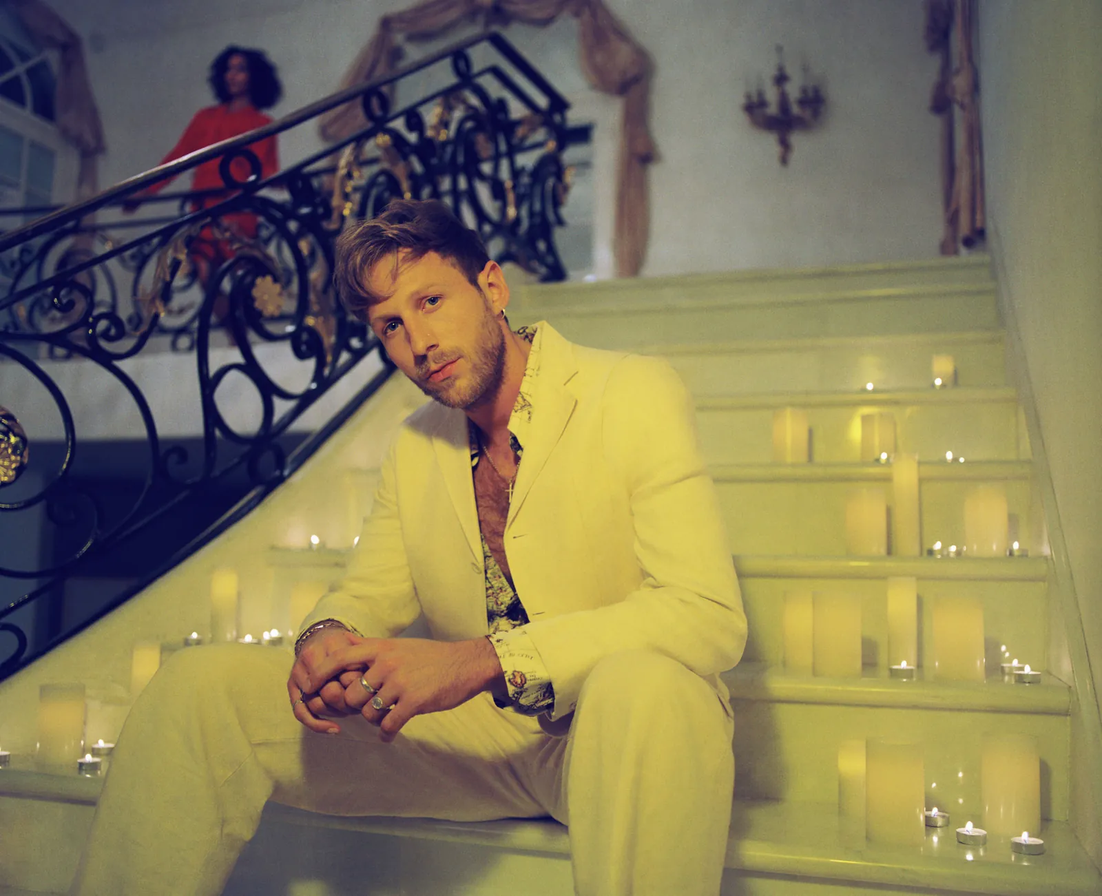 BURNS in a cream suit, seated on a candlelit staircase