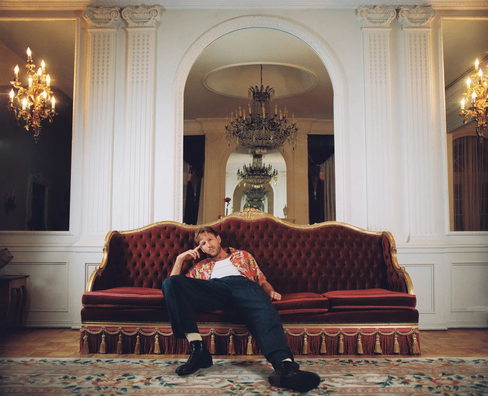 BURNS on a red velvet sofa beneath crystal chandeliers