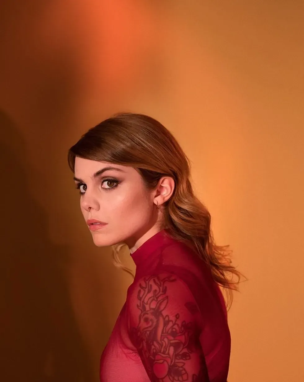 Coeur de Pirate looks over her shoulder, her tattoos visible through a sheer red sleeve