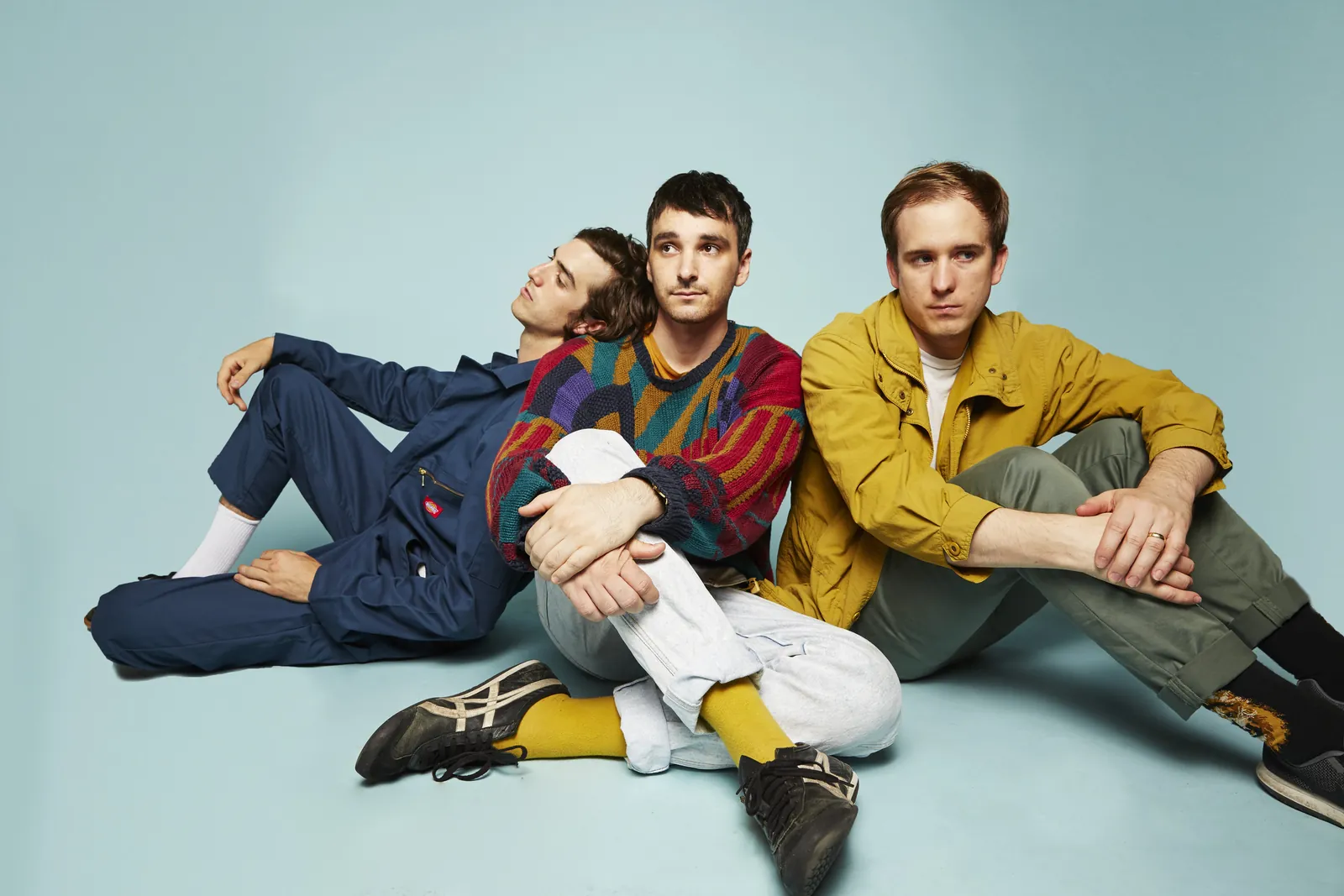 The three members of Half Alive sitting together on a pale blue floor