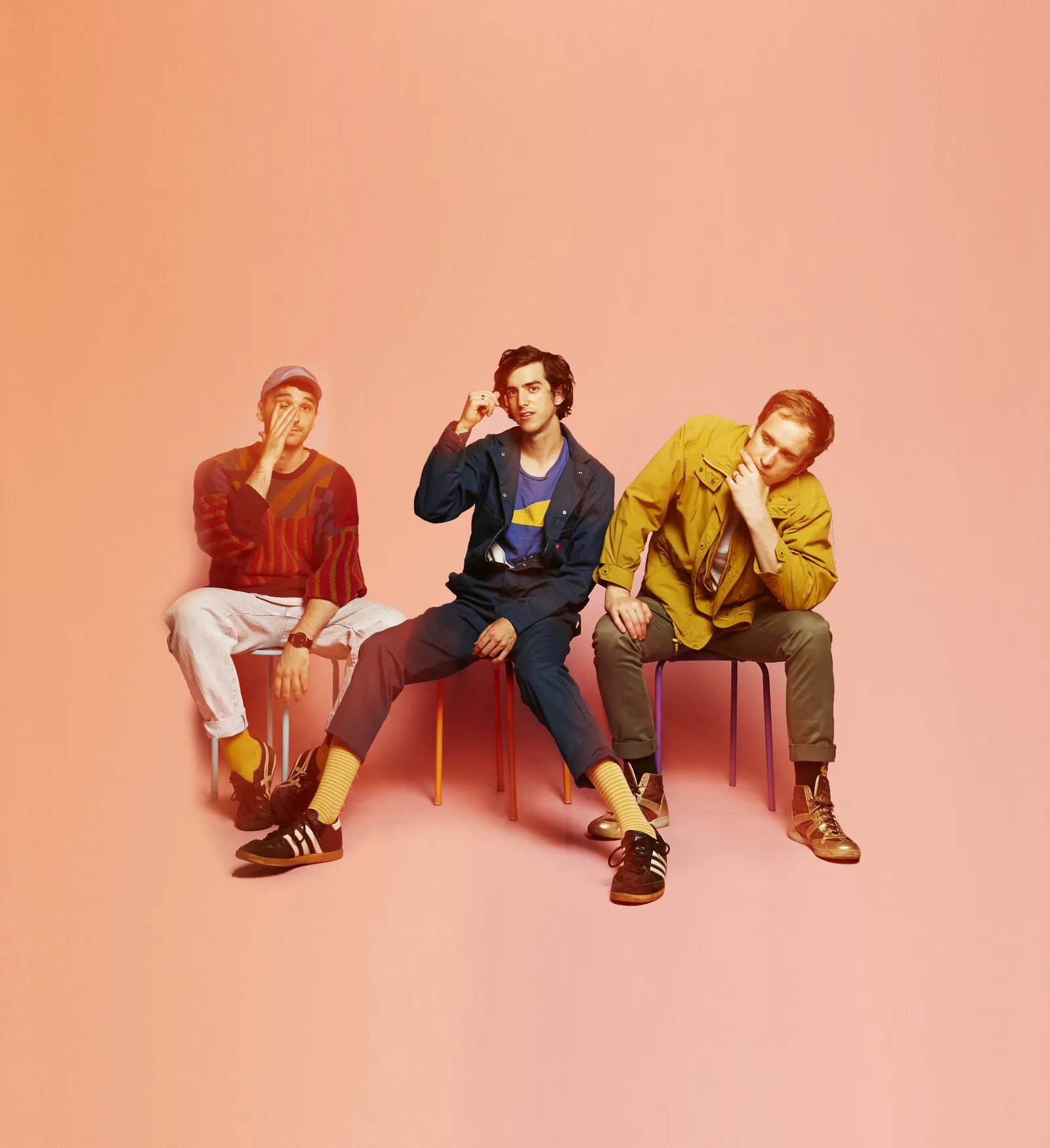 Half Alive seated on coloured stools against a peach backdrop