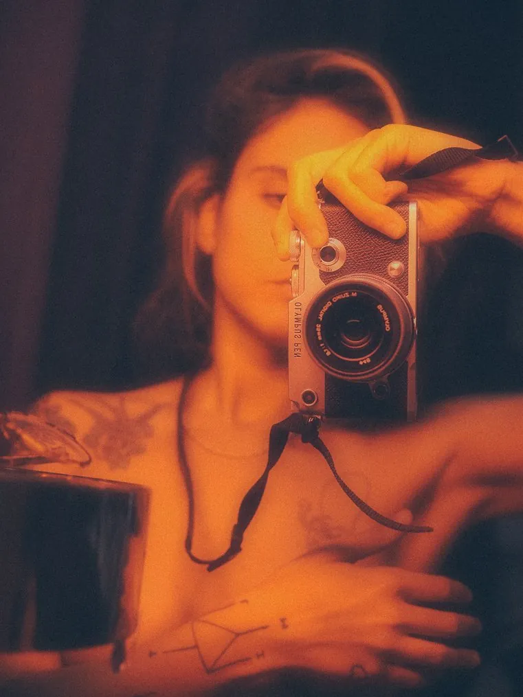 A woman holding a film camera, lit in orange