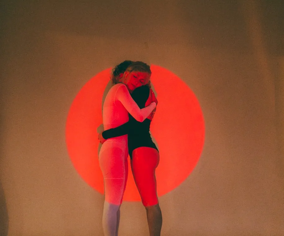 Two women embracing in front of a projected orange circle