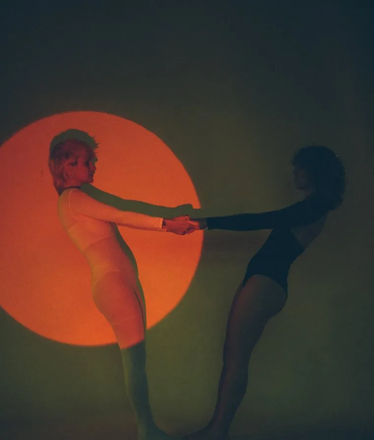 Two women holding hands across a projected orange circle